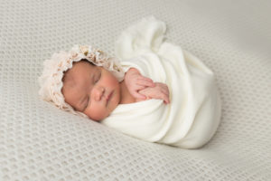 newborn girl swaddled in white with bonnet in studio session